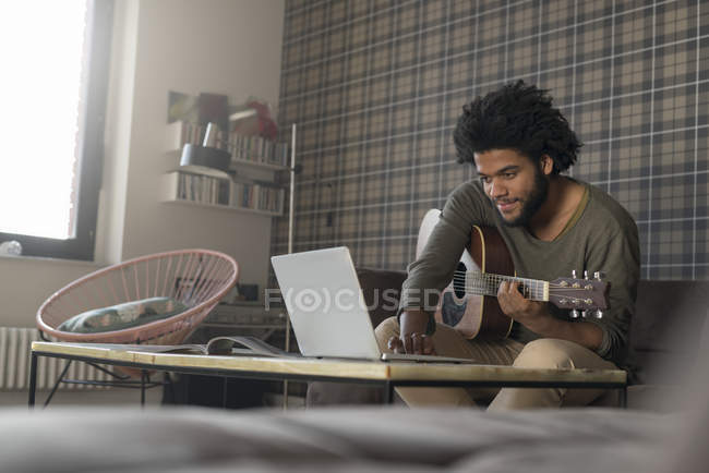 Людина грати на гітарі у вітальні — стокове фото