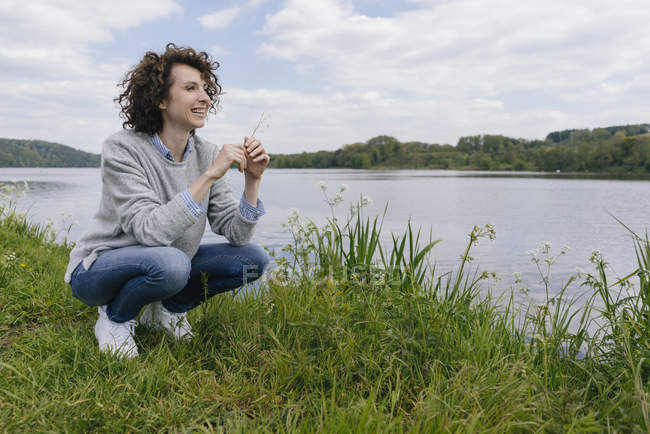 Donna accovacciata sulla riva del lago — Foto stock