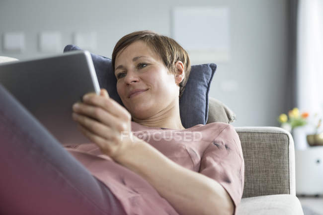 Жінка, лежачи на дивані, за допомогою планшетного ПК — стокове фото