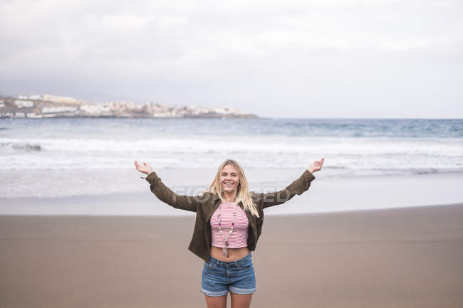 Портрет счастливой молодой женщины, стоящей на пляже с распростертыми руками — стоковое фото