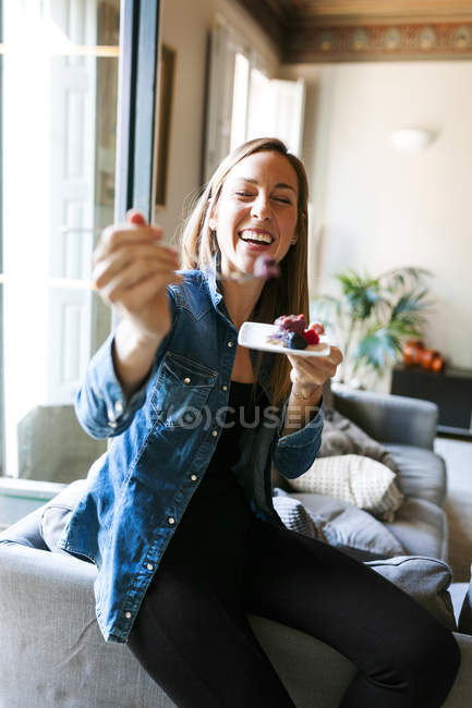 Abgeschnittenes Porträt einer lächelnden Frau, die Kuchen mit Beeren hält und Stück auf Gabel zeigt — Stockfoto
