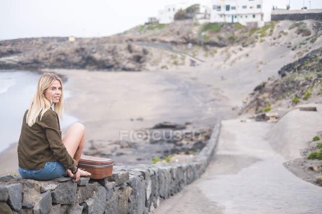 Espagne, Tenerife, jeune femme blonde assise sur un mur près de la plage — Photo de stock