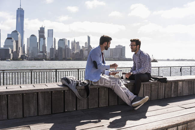 Dos hombres de negocios que trabajan en el paseo marítimo de Nueva Jersey con vistas a Manhattan, EE.UU. - foto de stock