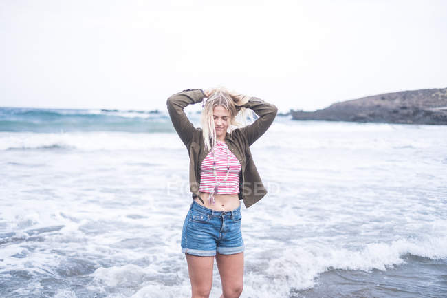 Junge blonde Frau steht am Strand — Stockfoto