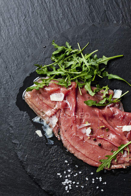 Closeup view of raw beef with rocket and cheese slices — Stock Photo