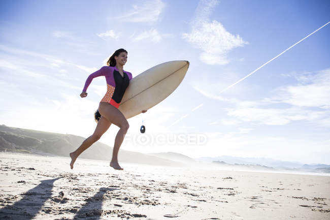 Young woman running at sandy beach with surfboard — Stock Photo