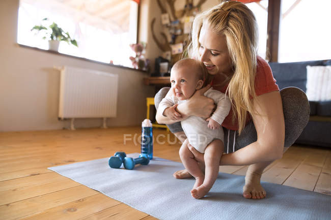 Smiling mother with baby and dumbbells at home — Stock Photo