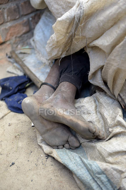 Голі ноги безпритульної людини, що спить під ганчірками — стокове фото
