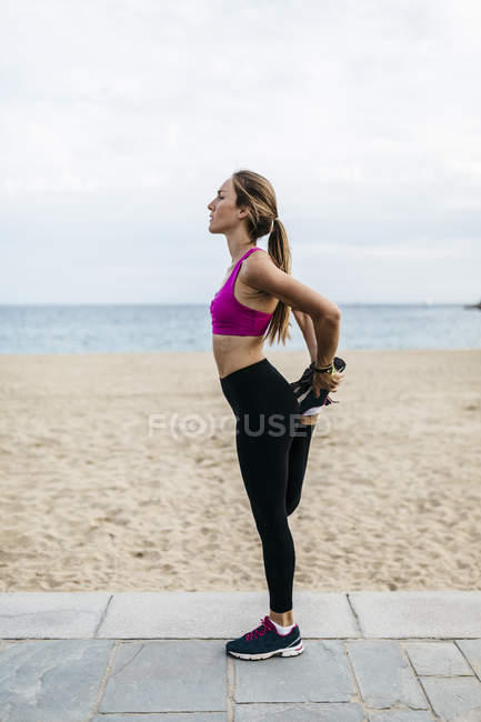 Jeune femme qui s'étire et se réchauffe pour s'entraîner à la plage — Photo de stock