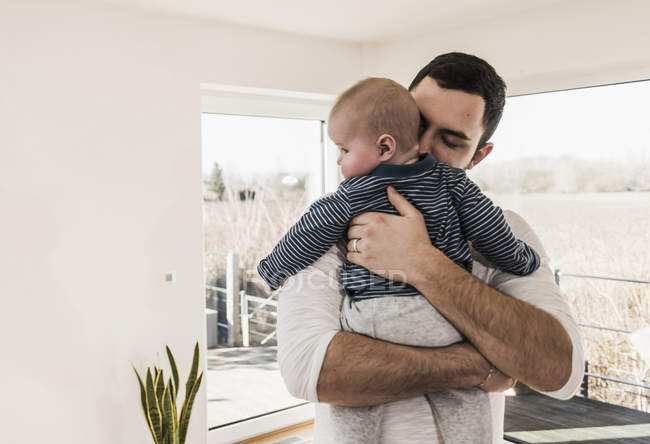Padre che stringe e abbraccia il bambino mentre sta in piedi in casa confortevole — Foto stock
