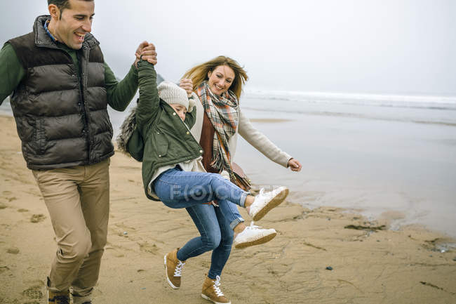Испания, Астурия, Счастливая пара, держащая за руки маленькую девочку во время прыжка на пляже — стоковое фото