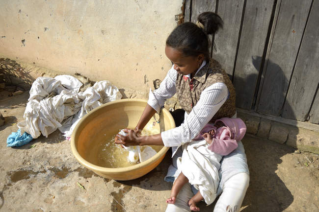 Madagascar, Fianarantsoa, Young mother with baby on lap washing laundry in a bowl — Stock Photo
