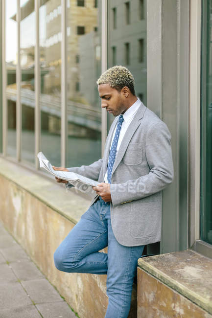 Businessman leaning against wall and reading newspaper — Stock Photo