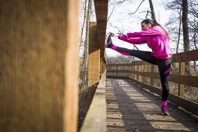 Femme s'étirant sur un pont en bois dans la forêt — Photo de stock