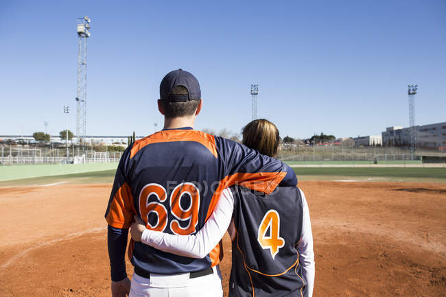 Rear view of male and female baseball player embracing on a baseball field — Stock Photo