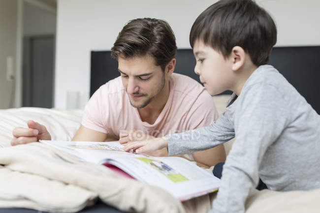 Feliz pai e filho lendo um livro na cama — Fotografia de Stock