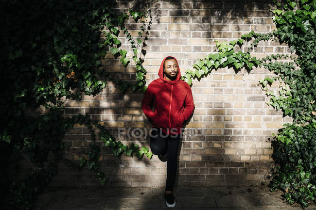 Portrait of young black guy in casual clothing, with the hood up, leaning against a wall. — Stock Photo