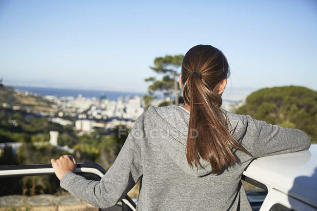 Молода жінка спирається на дах автомобіля на сонячному світлі і дивиться на вигляд — стокове фото