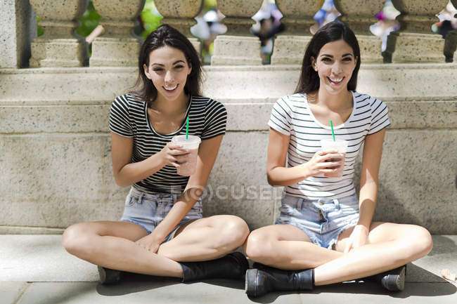 Portrait of two young women with drinks near stone fence — Stock Photo