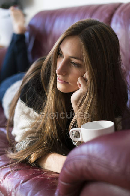 Mujer acostada en el sofá con una taza de café - foto de stock