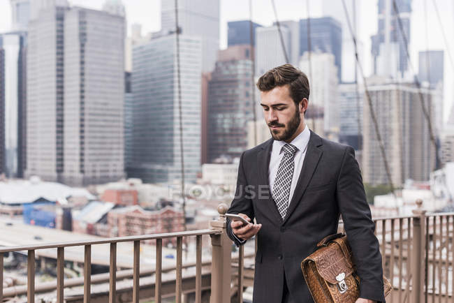 Usa, new york, brooklyn bridge, junger unternehmer am telefon, stadtbild im hintergrund — Stockfoto