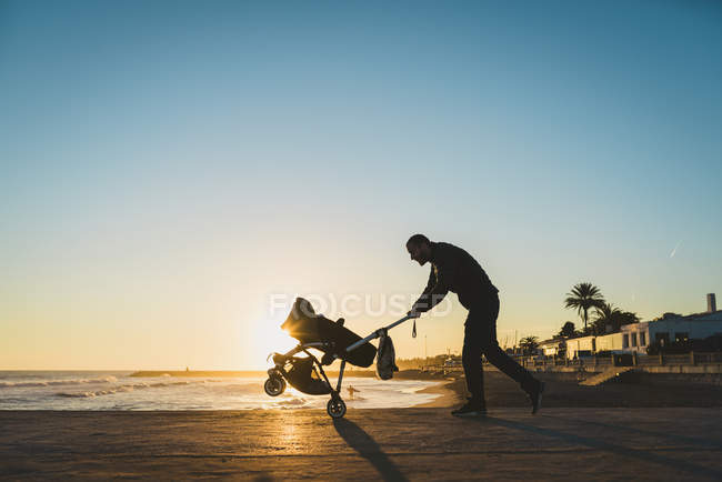 Чоловік ходить з коляскою на березі моря на заході сонця — стокове фото