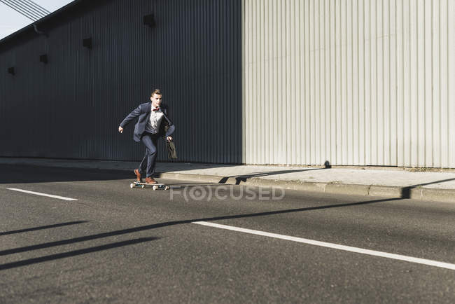 Jeune homme d'affaires à cheval skateboard dans la rue — Photo de stock