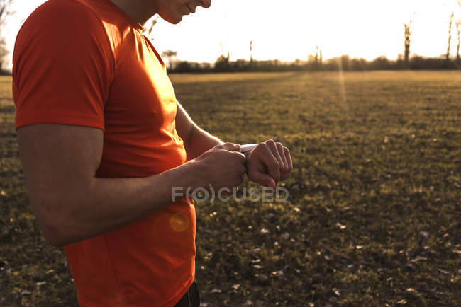 Обрезанный портрет молодого человека с помощью умных часов в поле — стоковое фото