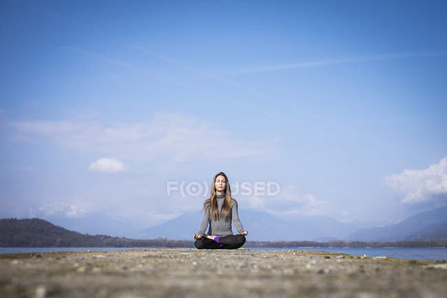 Femme pratiquant le yoga sur une jetée au bord d'un lac — Photo de stock