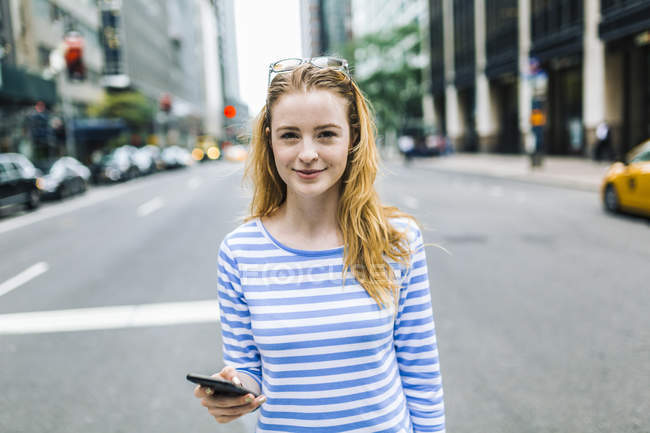 Jeune femme marchant dans la rue, tenant un téléphone portable — Photo de stock