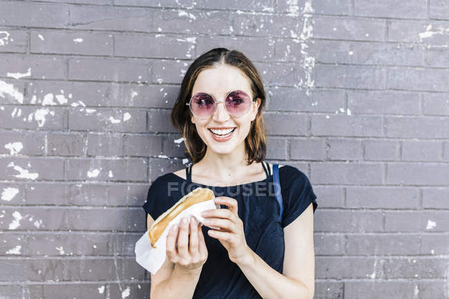 Primo piano di donna che mangia un hot dog davanti al muro — Foto stock