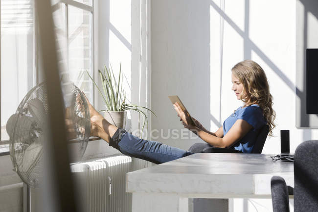 Випадкова бізнес-леді, використовуючи цифровий планшет з ногами на підвіконні в офісі — стокове фото
