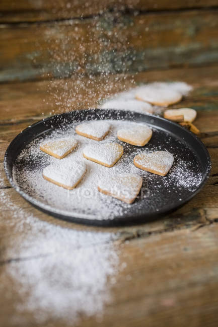 Sprinkling heart-shaped shortbreads with icing sugar — Stock Photo