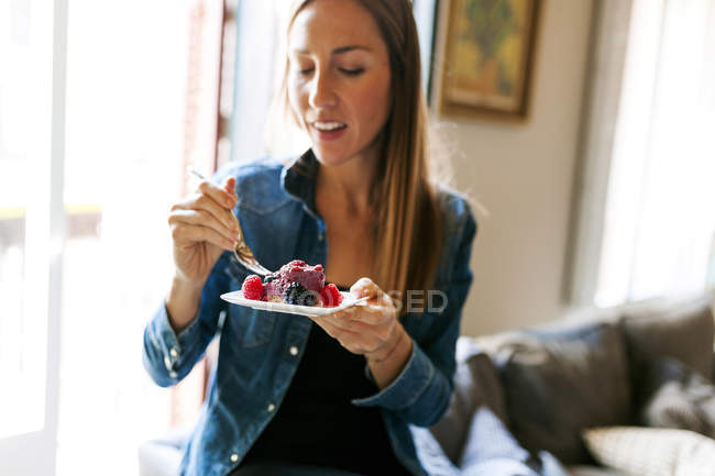 Cropped portrait of woman eating cake with berries indoors — Stock Photo
