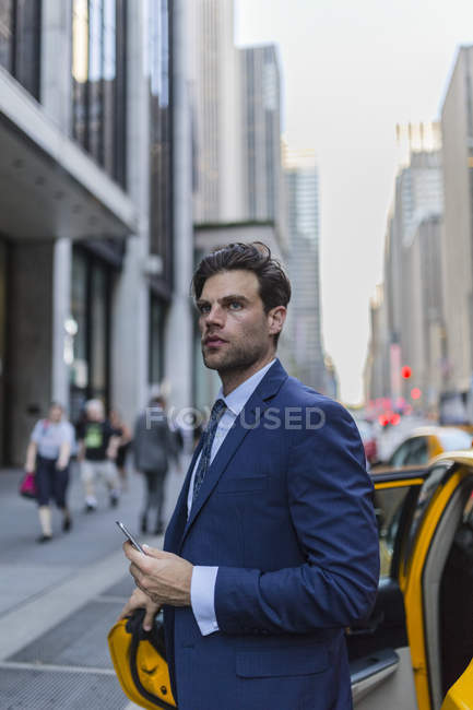 Ritratto di un uomo d'affari che lascia il taxi e tiene lo smartphone — Foto stock