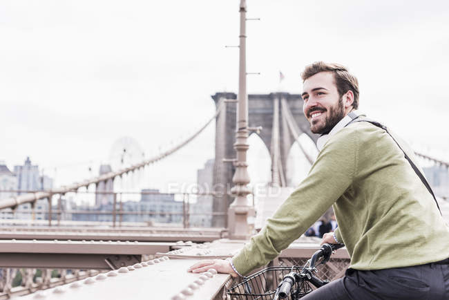 USA, New York, Ponte di Brooklyn, Giovane in bicicletta sorridente, guardando da parte — Foto stock