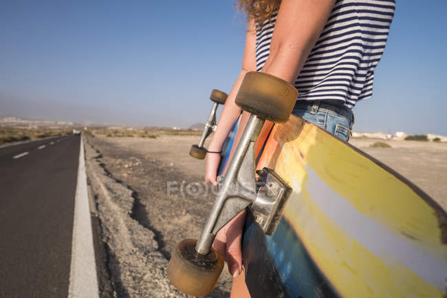 Femme avec planche à roulettes debout sur la route de campagne vide — Photo de stock