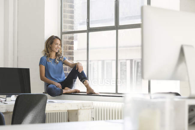 Casual businesswoman sitting on window sill in office — Stock Photo