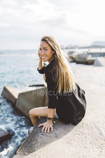 Retrato de una joven sonriente sentada frente al mar - foto de stock