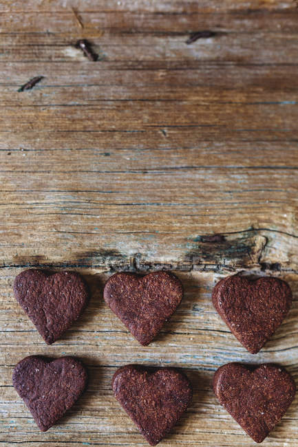 Homemade heart-shaped chocolate cookies in rows on wood — Stock Photo