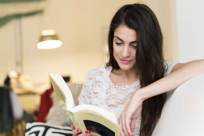 Жінка сидить на дивані і читає книгу — стокове фото