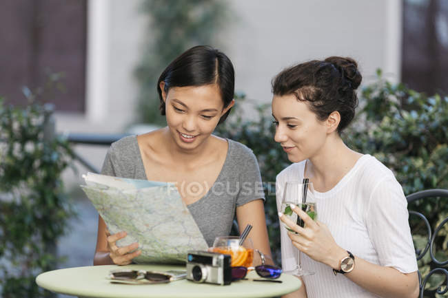 Deux jeunes femmes regardant ensemble la carte au café sur le trottoir — Photo de stock