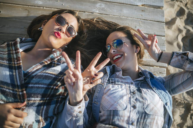 Porträt zweier junger Frauen, die auf Holzdeck liegen und lustige Gesichter machen — Stockfoto