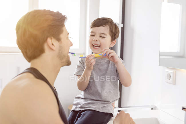 Счастливые отец и сын чистят зубы вместе в ванной комнате — стоковое фото