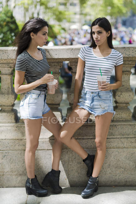 Portrait of two young women holding drinks near stone fence — Stock Photo