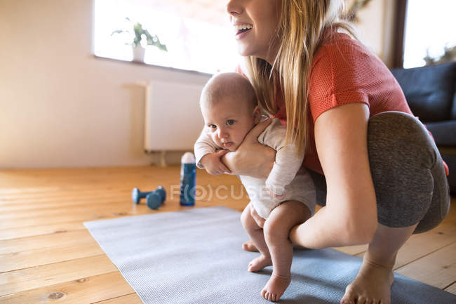 Mère souriante avec bébé et haltères à la maison — Photo de stock