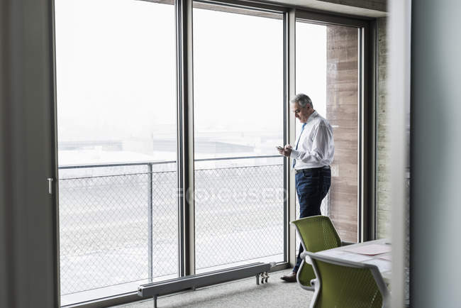 Gerente de pé no escritório e segurando smartphone — Fotografia de Stock