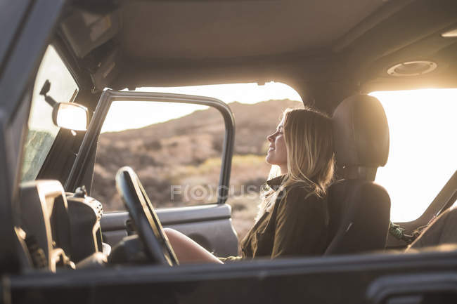 Young blond woman sitting in car at sunset — Stock Photo