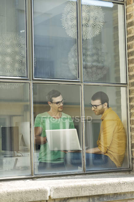 Young professionals at the window using laptop — Stock Photo