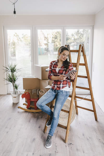 Зрелая женщина, опирающаяся на лестницу и пользующаяся планшетом в новом доме — стоковое фото